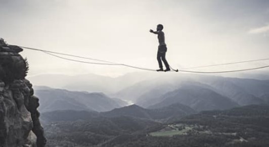 Person tightrope walking across a canyon in a mountainous region